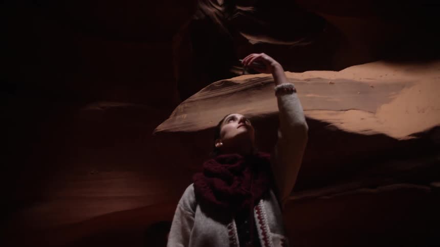 A woman stands in a dark cave holding up her cell phone and looking at it