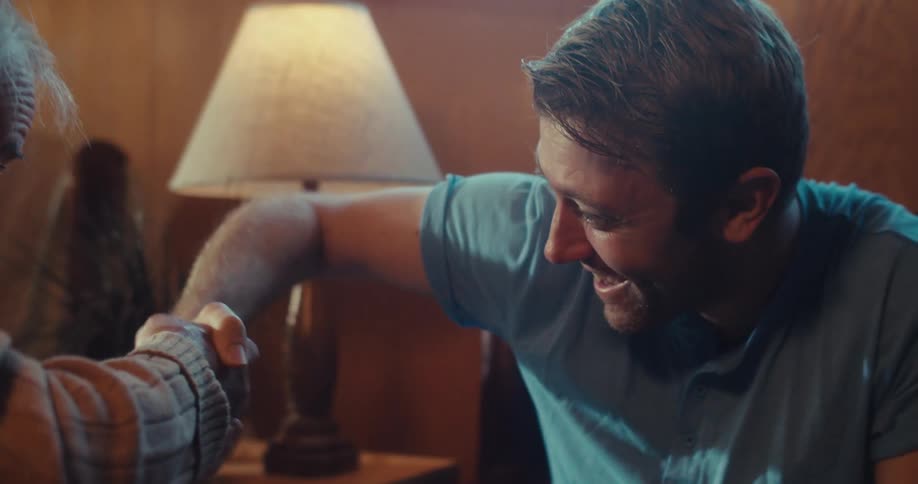 A young man teaches an elderly man a funny handshake at home both smiling with happiness