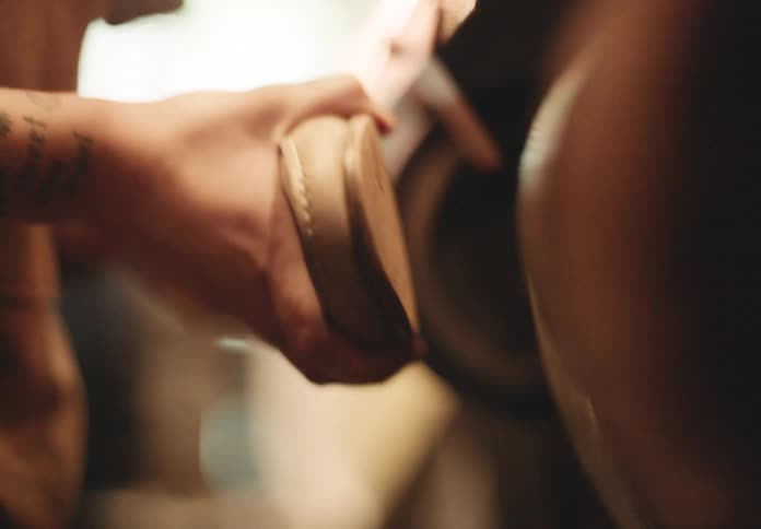 A shoemaker sands the sole of a shoe using a large spinning sanding machine