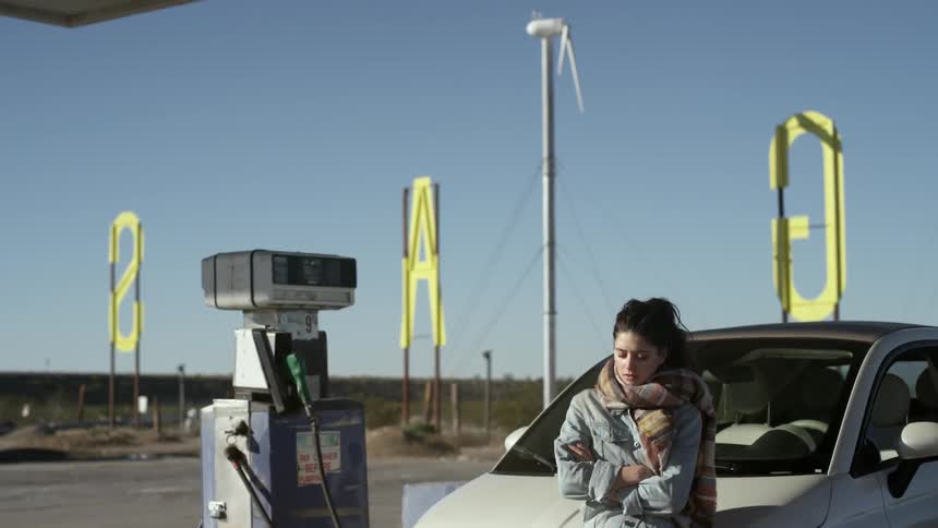 A woman leaning on a car at a gas station