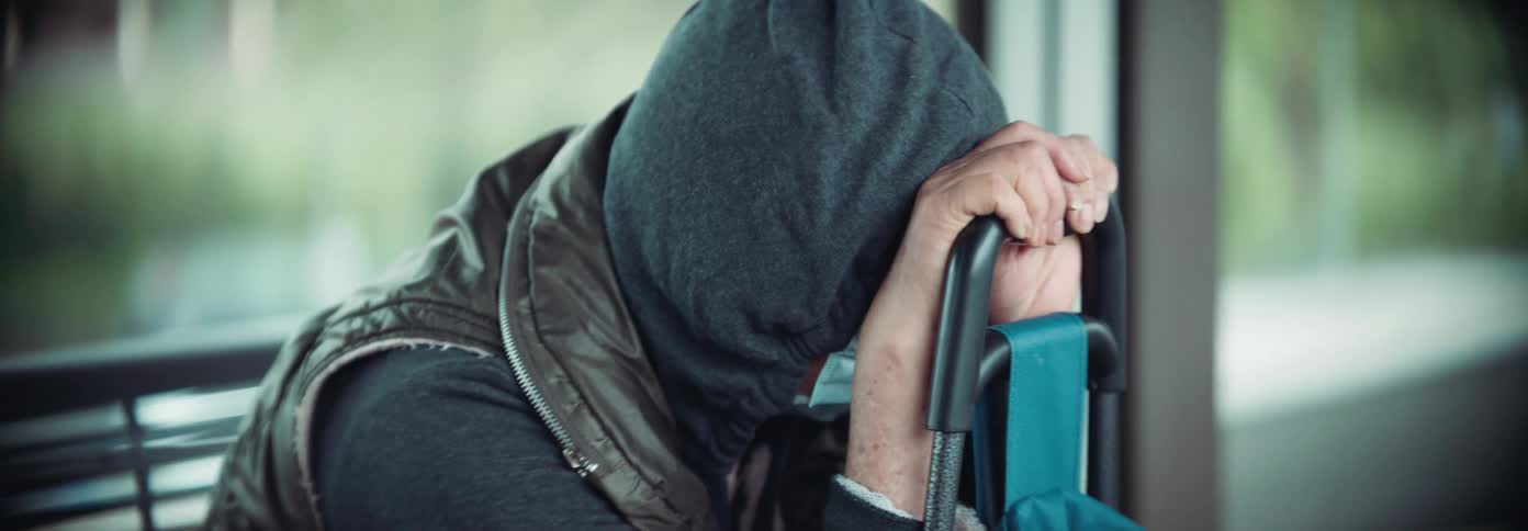 A person wearing a hooded jacket and vest rests their head on their hands while seated