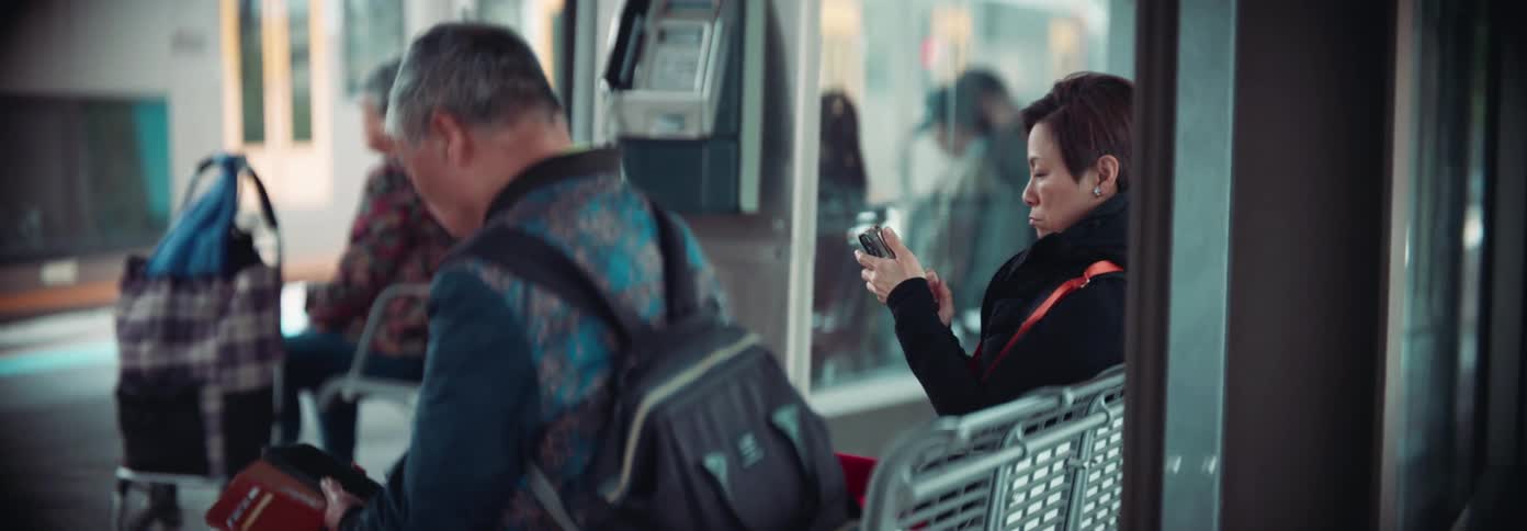 A man and a woman sitting at a train station both using their phones