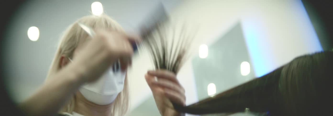 A masked hairstylist is cutting a clients hair in a salon