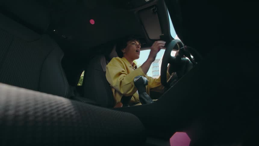 View from the passenger floorboard of a happy woman driving a car in the daytime.