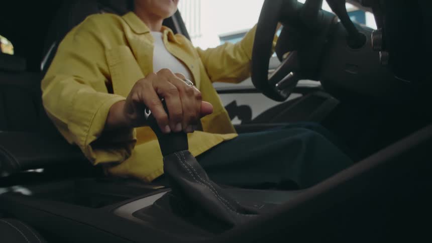 Low angle view of a smiling woman in a yellow jacket who is shifting gears while driving a car