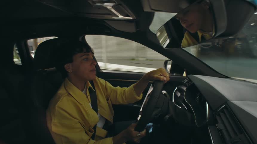 A woman dances and sings along to a song as she drives along a city street during the day