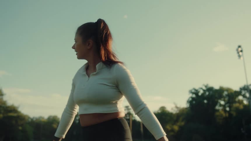 Three women are stretching and smiling on a football field during golden hour