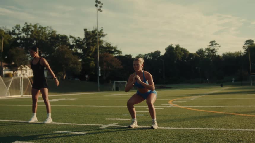 Two women exercise on a sports field during the day