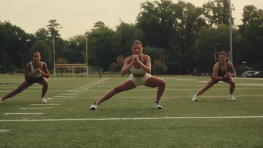 A group of women exercise together on a field at dusk