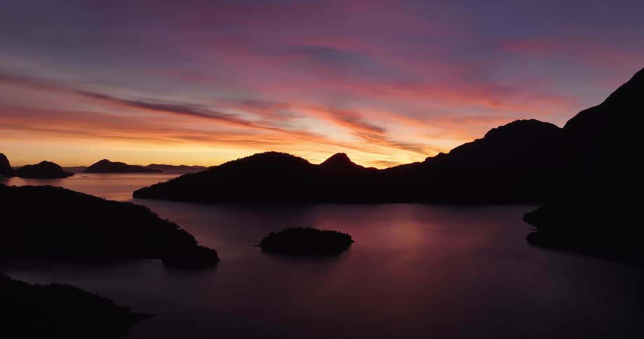 Mountains and islands stand silhouetted against a cloudy red sky