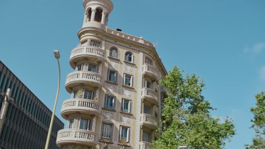 A view from inside a car passing by shows the Casa Antonia Serra i Mas, an old ornate building with a tower situated at a busy intersection in Barcelona, Spain