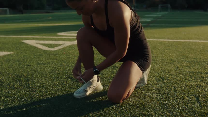 Woman crouching on a grass sports field tying her shoelaces