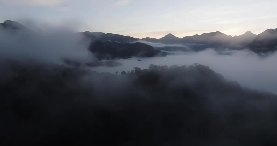 Aerial shot of a misty mountain range at dawn with clouds rolling over the peaks