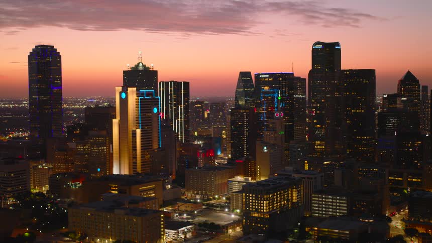 Dusk aerial of downtown dallas with lit skyscrapers and an orange sky