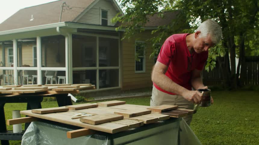 A man paints his wooden shutters in front of a house
