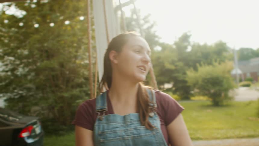 A woman relaxes and smiles while gently swinging outside her house