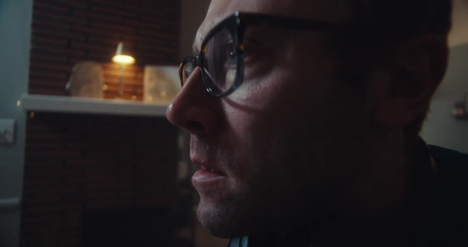 A fairskinned man with reddishblonde hair and glasses wearing headphones and a blue shirt sits at a desk with a computer his expression showing surprise or apprehension