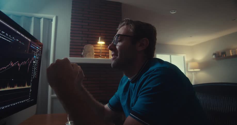 A man smiles and clenches his fist in excitement while watching stock market data on his computer