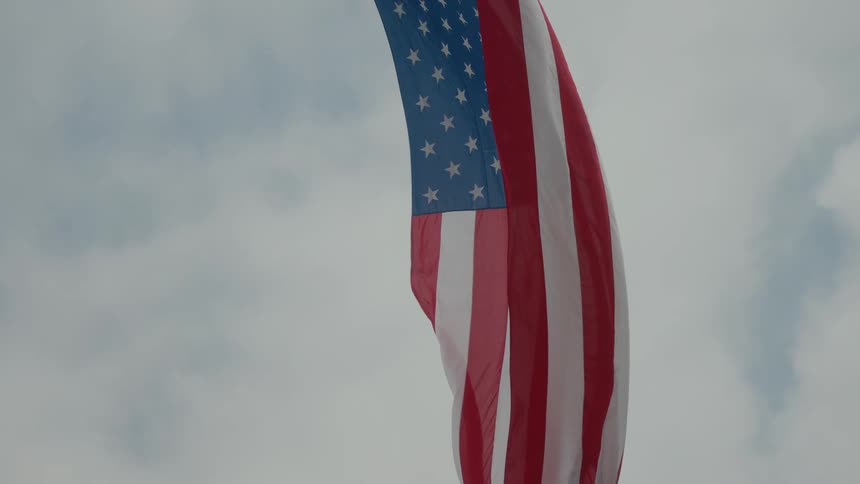 An american flag flying midair in the wind with a cloudy sky in the background