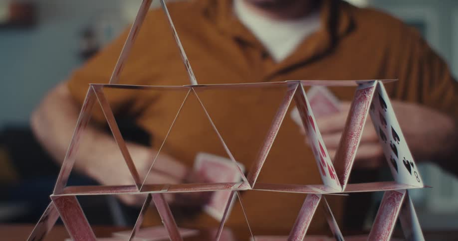 A man is carefully placing playing cards in a triangle atop a card tower two stories high