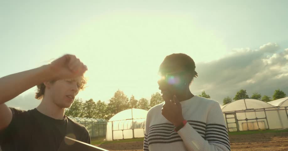 Two agriculture students in a field discuss their work while using a laptop
