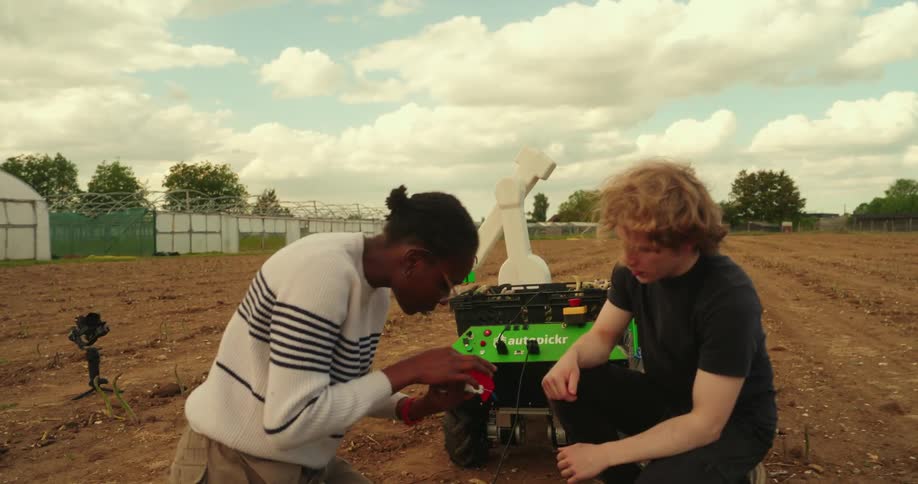 A man and woman work on a robot on a farm