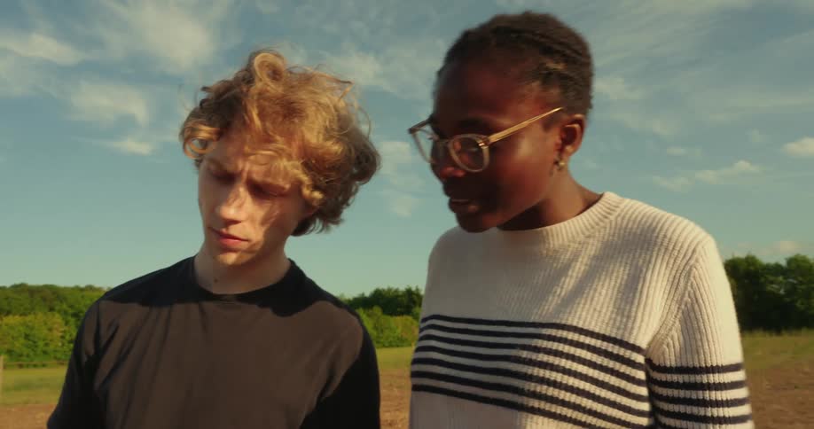 Two people stand in a field discussing work while one of them holds a laptop