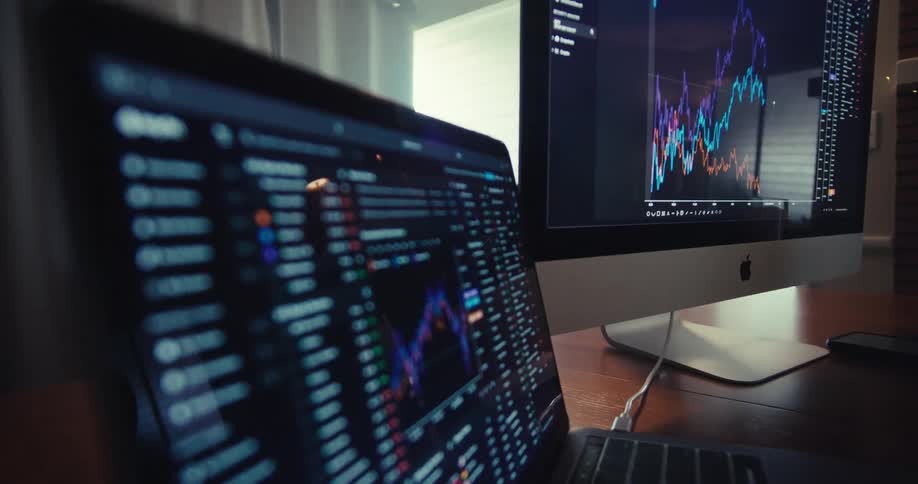 Computer monitors on a desk are displaying graphs