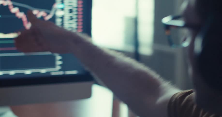 A man wearing headphones and analyzing a stock chart on a monitor