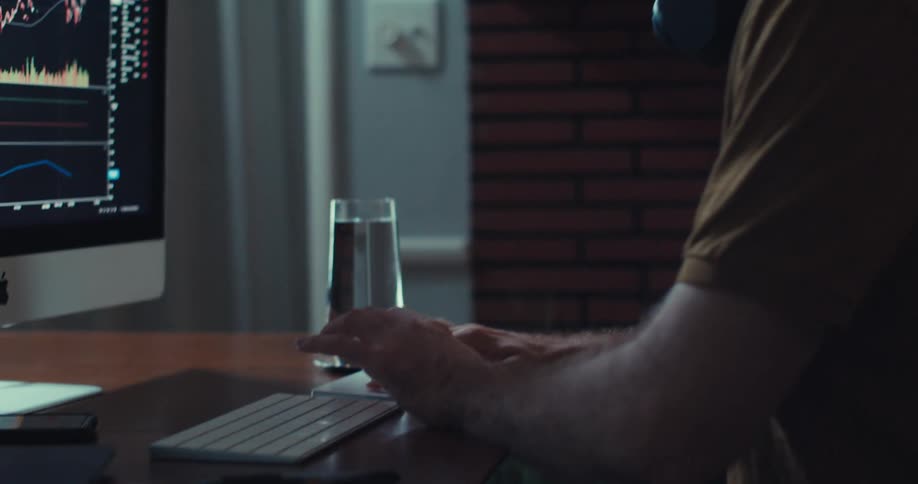 Close up of a man operating a desktop keyboard and touch pad while trading on a monitor