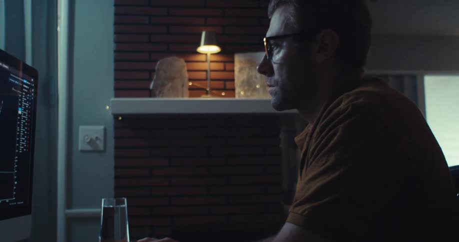 A man sits indoors while using a track pad and looking at a computer monitor