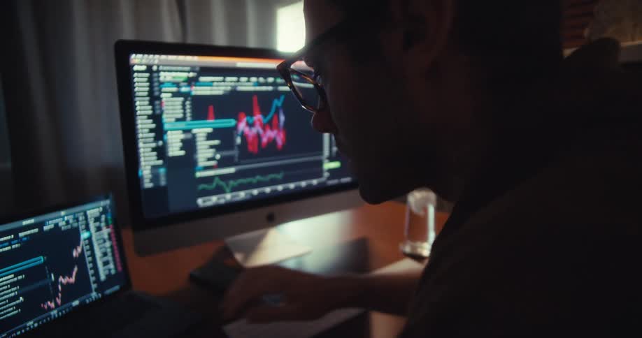 A man types on his laptop while looking at line graphs