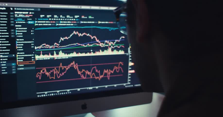 A young man wearing glasses watches the stock market on his computer screen