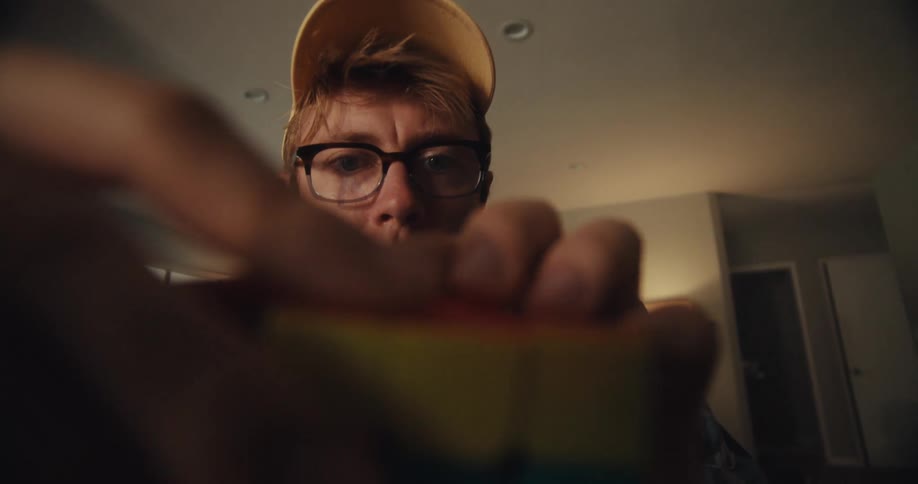 A man intently solves a rubiks cube while looking closely at it indoors