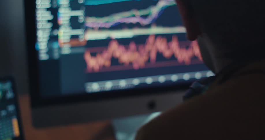 A man analyzes stock market data on a computer screen filled with charts and graphs