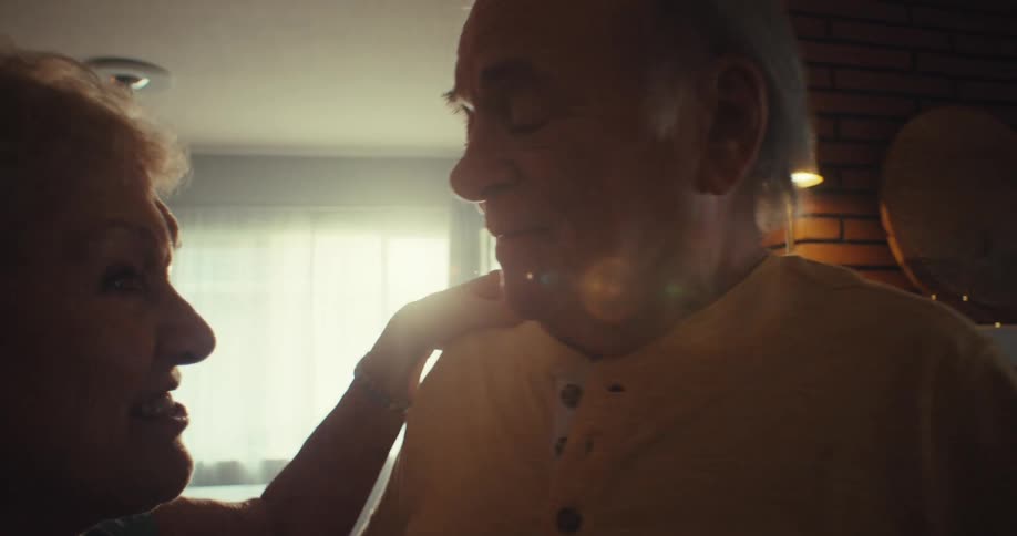 Elderly man and woman hold hands while dancing indoor at dawn