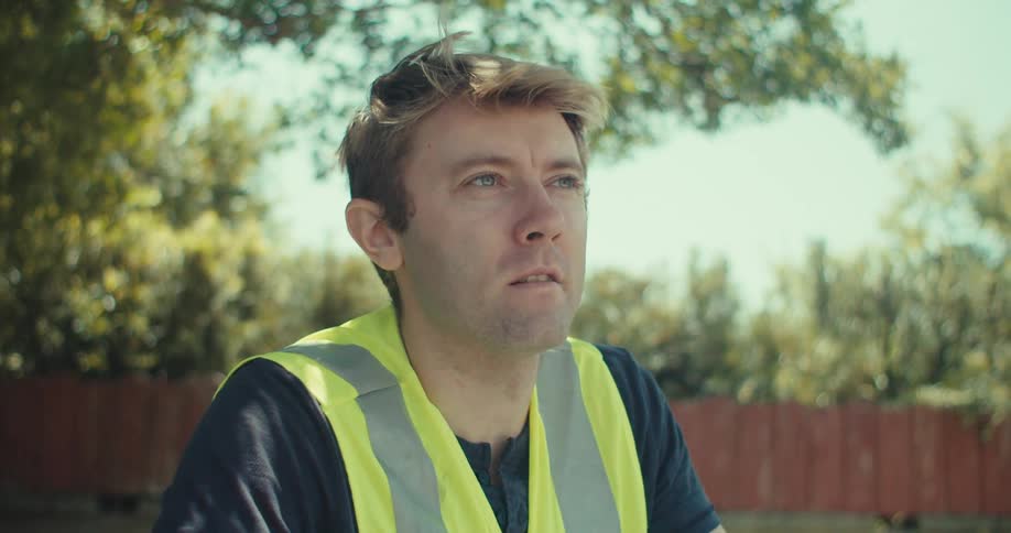 A construction worker sits outdoors in nature thoughtfully planning on a chart