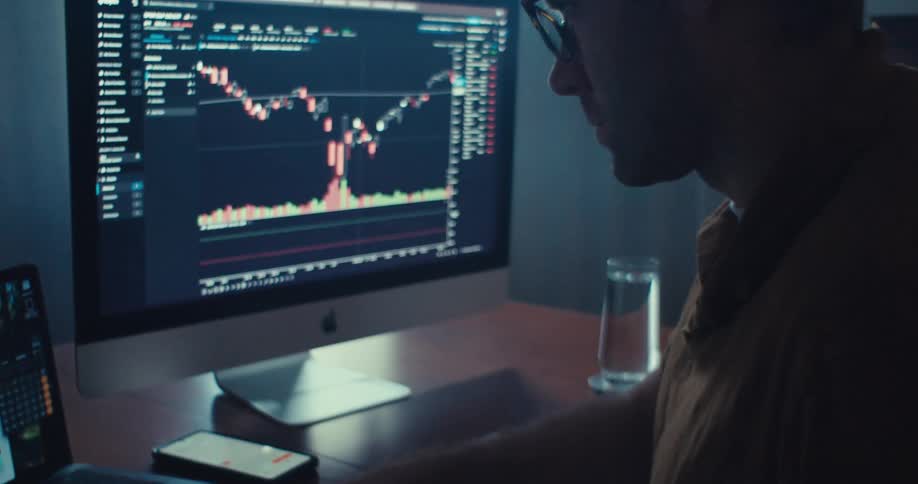 A person is analyzing stock market data on a laptop while taking notes