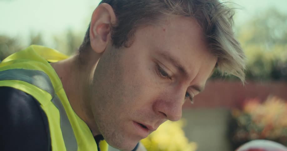 A man in green vest writing on a book while sitting at the yard during the day