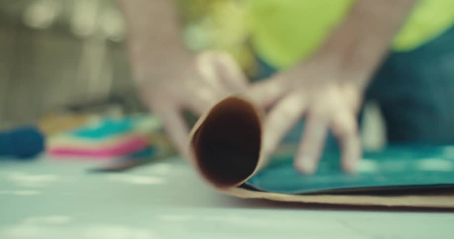 A worker spreads out a large blueprint on a table in a sunlit backyard