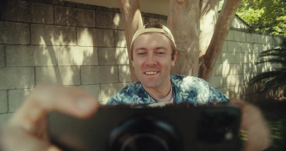 A man waves at the cell phone as he films in the yard