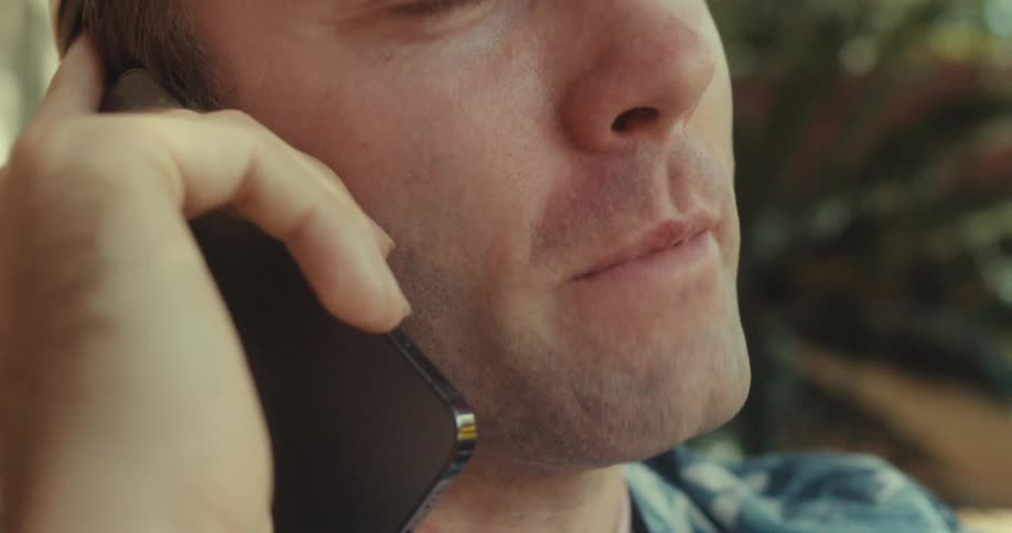 A man smiles while talking on his phone outside