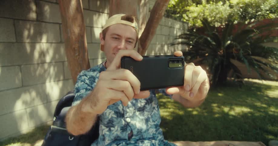 Man makes a horizontal phone recording while sitting under a tree in daytime