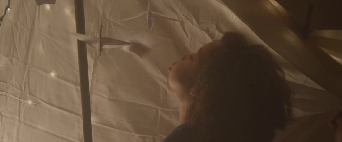 Child blowing at hanging paper origami cranes