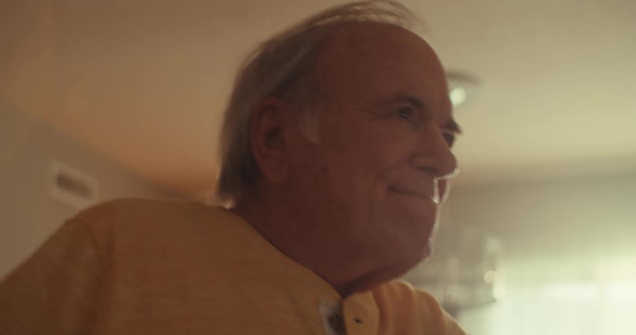 An elderly man dances joyfully alone inside a cozy room