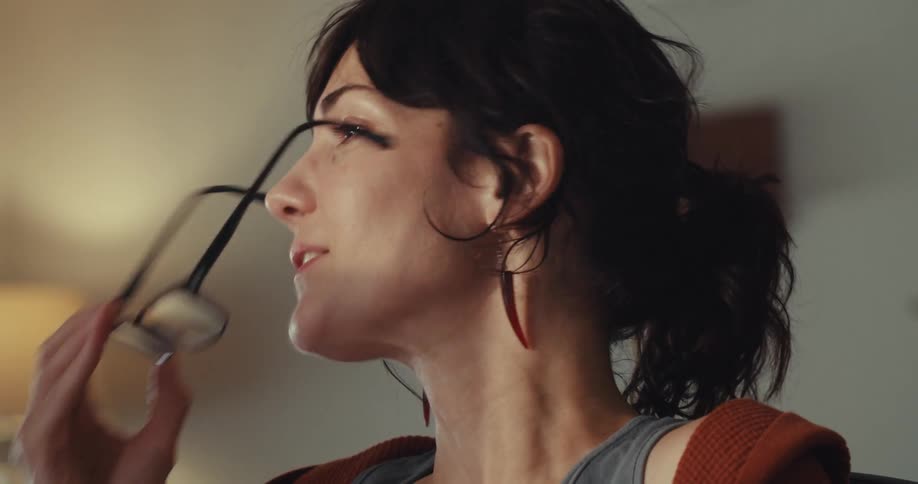 A woman removes her glasses and rubs her nose