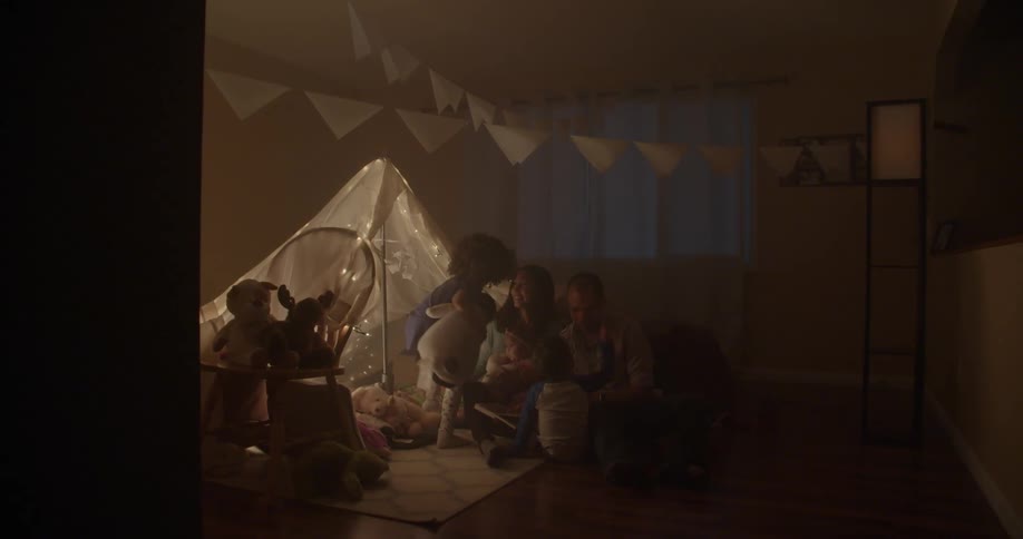 Young child carrying a doll runs into a room to sit with a man and woman that are sitting on the floor