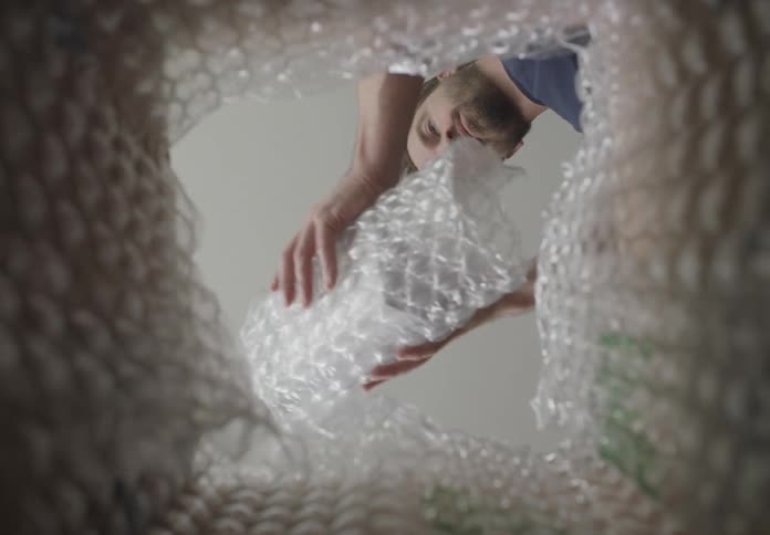 Point of view man wrapping box with bubble wrap then placing in box lined with bubble wrap