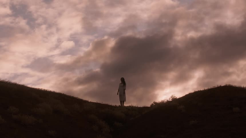 Woman standing on ridge of a hillside at sunrise