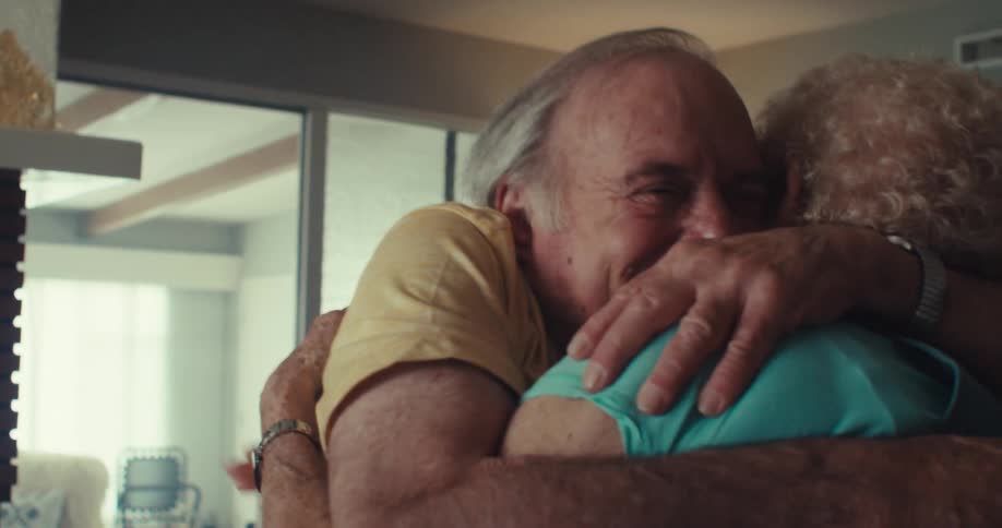 An elderly couple shares an animated conversation and embraces warmly